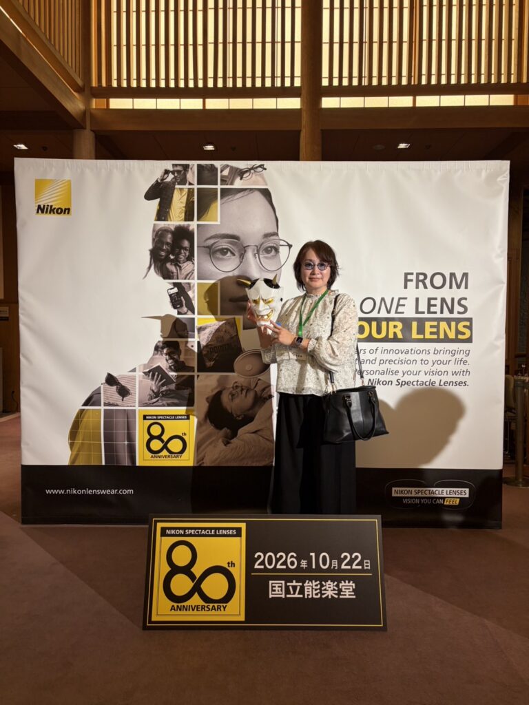 ニコンメガネレンズ80周年記念パネルの前に立つ当社スタッフ